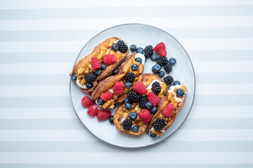 Fresh sweet rolls with cream cheese and fresh blueberries, strawberries, raspberries and currants on a white plate on a white-grey stripped surface. Copyspace, place for your text.