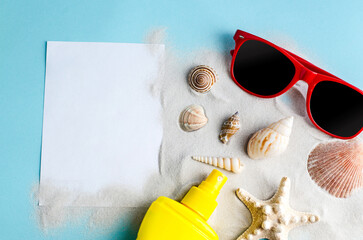 Seashells, sand, sunscreen and glasses, sheet of paper on a blue background with space for text.