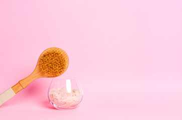 Sea salt and a wooden brush for dry massage on a pink background