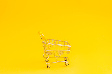 Miniature shopping trolley on a yellow background with place for text.