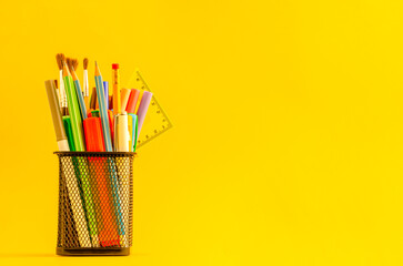 Black cup with items for school on a yellow background with place for text.