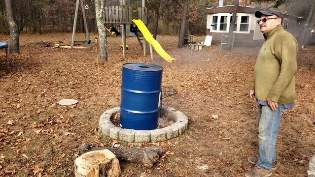 Men check the fire pit while burning wood inside the blue barrel to remove the paint. This barrel will be used to make traditional smoker.