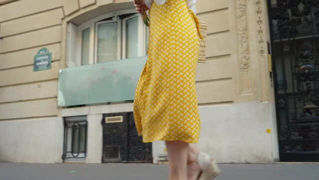 A young girl in a yellow skirt with a bouquet of roses walking towards the Eiffel Tower