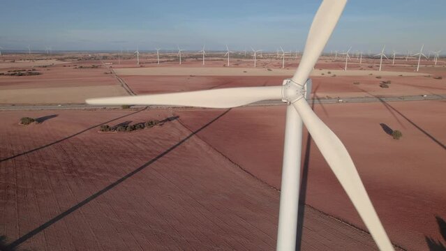 Elevated view of a wind turbine farm with a close-up of a wind turbine spinning as seen from the nacelle at sunset. Group of windmills are turning in the background. Cuenca, Castilla La Mancha, Spain