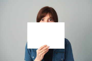 sheet of white paper held in front of the girl's face. with empty space for text or image, mockup