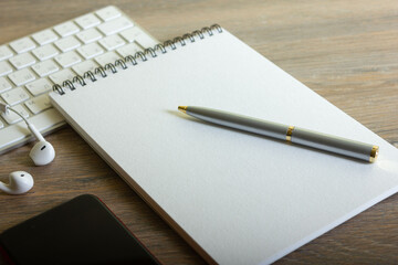 Notepad with pen and keyboard on wooden table with headphones and smartphone