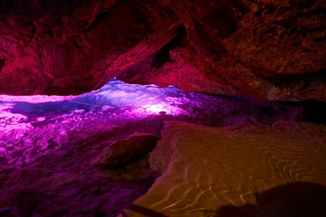Dark cave view from inside with a lumen. Stalactites and stalagmites inside the stone grotto. Colorful stones in the cave. Lighting electricity beauty of the cave.