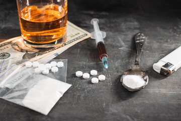 Alcohol drink in a glass, syringe with a dose of drugs, white pills in a transparent bag, narcotics powder in a spoon and US dollar cash on dark background. Concept of addiction and bad habits