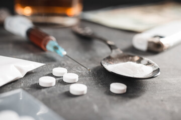 White pills, syringe with a dose of drugs, narcotics powder in a spoon and US dollar cash on dark background. Concept of addiction and bad habits
