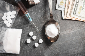 Fototapeta na wymiar White pills, syringe with a dose of drugs, narcotics powder in a spoon and US dollar cash on dark background, top view. Concept of addiction and bad habits