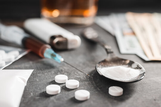 White pills, syringe with a dose of drugs, narcotics powder in a spoon and US dollar cash on dark background. Concept of addiction and bad habits