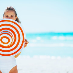 Happy young woman in swimsuit hiding behind beach hat