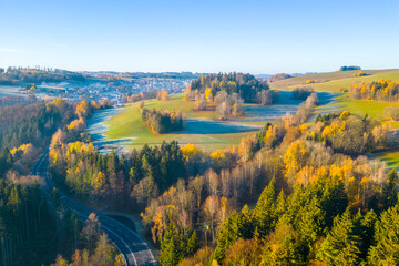 Aerial view of sunny, hilly and forested landscape illuminated by autumn sun. Asphalt road cutting through the scenery. Aerial view from drone.