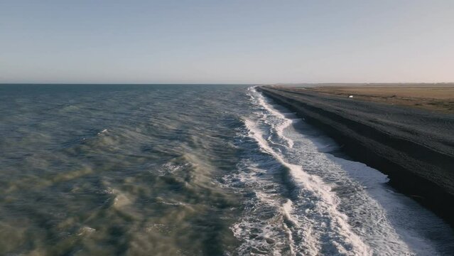 Waves rolling ashore a picturesque empty beach at sunset, aerial parallel tracking shot