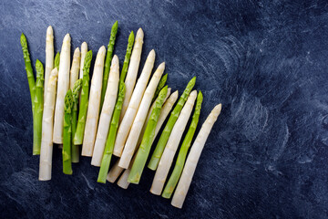 Frischer roher weißer und grüner Spargel angeboten als Draufsicht auf einem grauen Board mit...