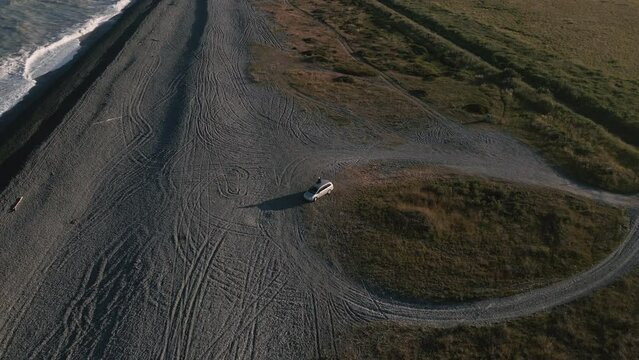 Car on a picturesque beach during magnificent sunset; revealing aerial pull away shot