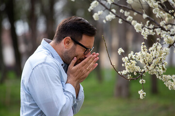 Man sneezing beside blooming tree