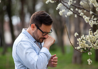 Man sneezing beside blooming tree