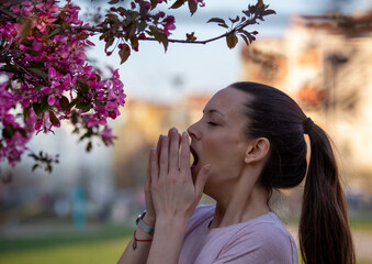 Girl sneezing in napkin in front of blooming tree in spring