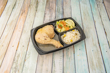 A grilled chicken thigh in sauce with rice and salad in a delivery container