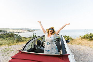 Happy woman sitting in white convertible car with beautiful view and having fun - travel summer vacation and rental car concept