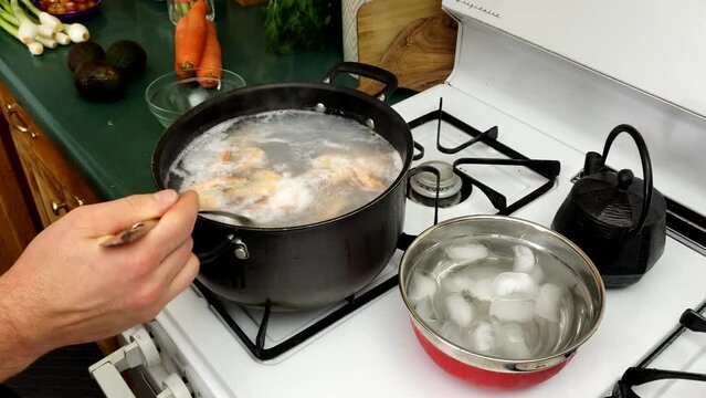 Removing cooked medium size shrimps from pot of boiling water into bowl with ice water to quickly cool down sea food
