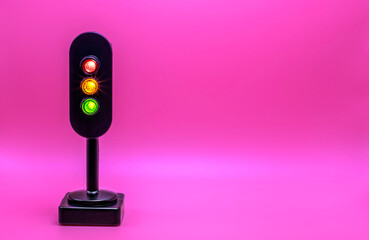 Miniature traffic light with red, orange and green light on. Studio shot. Pink empty background.