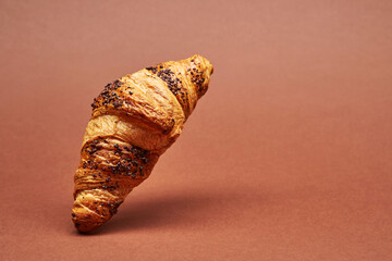 Croissant raised above surface of the bright solid fond plain red-brown background