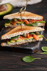 Two club sandwiches with salmon, avocado, capers, cream cheese and baby spinach leaves on vintage wooden cutting board