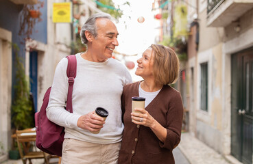 Cheerful Senior Couple Walking With Backpack Drinking Coffee Outside