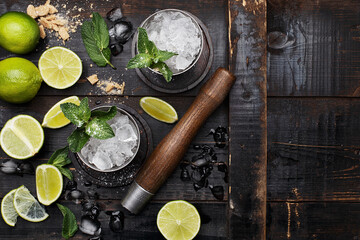 Mojito cocktail with lime, mint and crushed ice on dark vintage wooden background. Top view with copy space