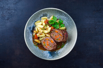 Traditionelle slow cooked deutsche Wagyu Rinderrouladen mit Gnocchetti-Sardi Nudeln in würziger Bratensoße als Draufsicht auf einem Nordic Design Teller mit Textfreiraum