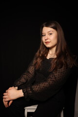 portrait of a beautiful young brunette woman in a black blouse on a black background. strict portrait of a girl on a black background