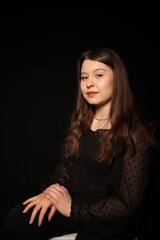 Naklejka premium portrait of a beautiful young brunette woman in a black blouse on a black background. strict portrait of a girl on a black background