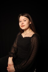 portrait of a beautiful young brunette woman in a black blouse on a black background. strict portrait of a girl on a black background