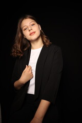 Obraz premium portrait of a beautiful young brunette woman in a black blouse on a black background. strict portrait of a girl on a black background