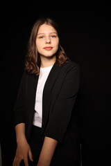 portrait of a beautiful young brunette woman in a black blouse on a black background. strict portrait of a girl on a black background