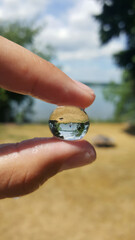 hand with clear marble orb refracting lake scene behind