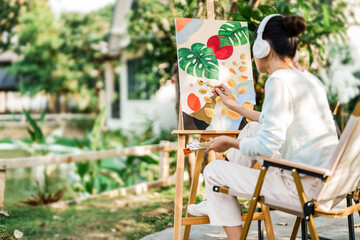 Young asian woman artist painting on canvas..Female artist drawing with inspiration in garden.
