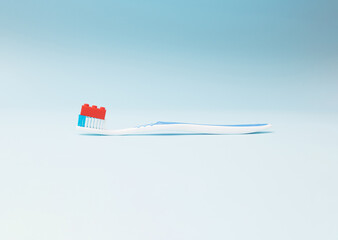 A blue and white toothbrush with a small red block toy on it.