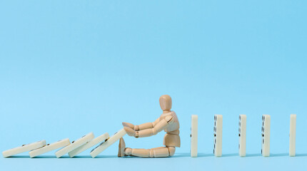 A wooden puppet toy holds back a falling domino on a blue background, representing the concept of a strong personality