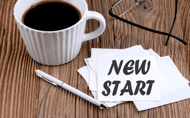 NEW START text on sticky with coffee and pen on wooden background