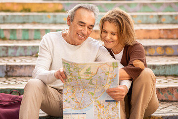 Fototapeta premium Happy Senior Couple Planning Vacation Holding Touristic Map Sitting Outside