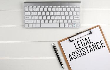 Home office workspace with keyboard, clipboard and pen with text LEGAL ASSISTANCE on white wooden background , business concept