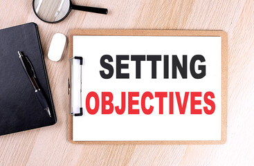 SETTING OBJECTIVES text on clipboard on wooden background
