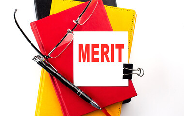 MERIT text written on a sticky on colorful notebooks