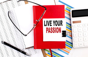 LIVE YOUR PASSION text on sticky on notebook with chart, calculator and pen