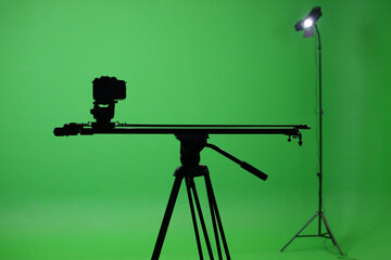 Film studio with a green screen. Tripod with camera, and rails. Shooting studio with green room. Chromakey green background.