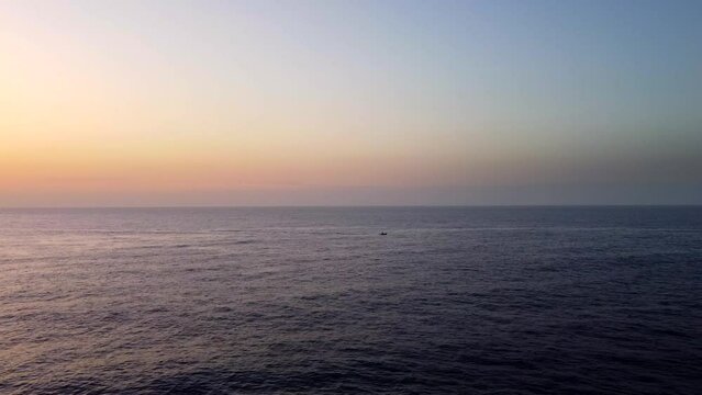 Small boat sailing on ocean at sunrise. Drone tracking ship at sea