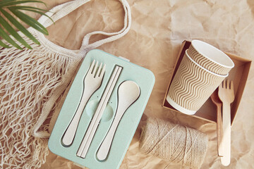 Ecological sustainable tableware cutlery, cardboard cups made from natural materials and reusable bag on crumpled paper. Zero waste lifestyle.